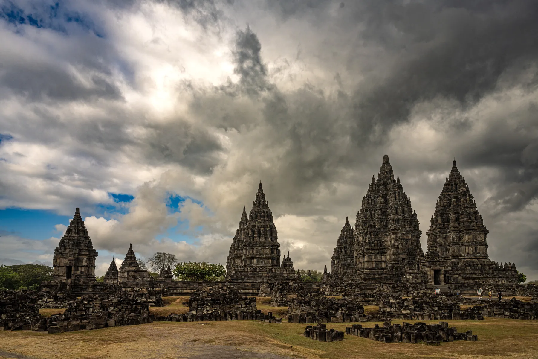 Kamienne wieże świątyń Prambanan pod rozświetlonymi chmurami.